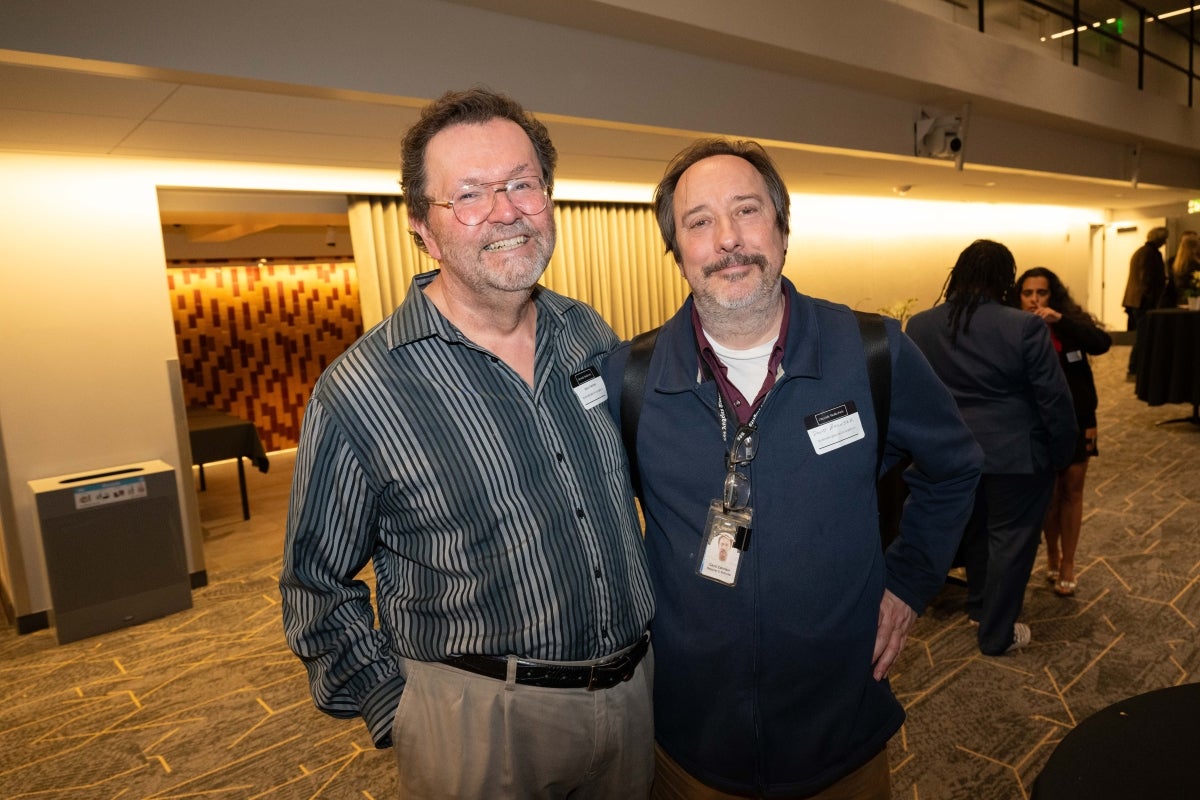 Two men with name tags pose for a photo in a lobby