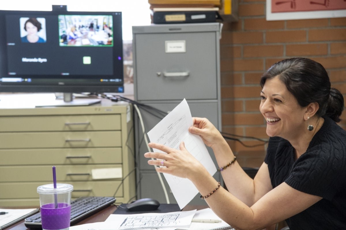 Woman seated at a table holding up a peice of paper and smiling.