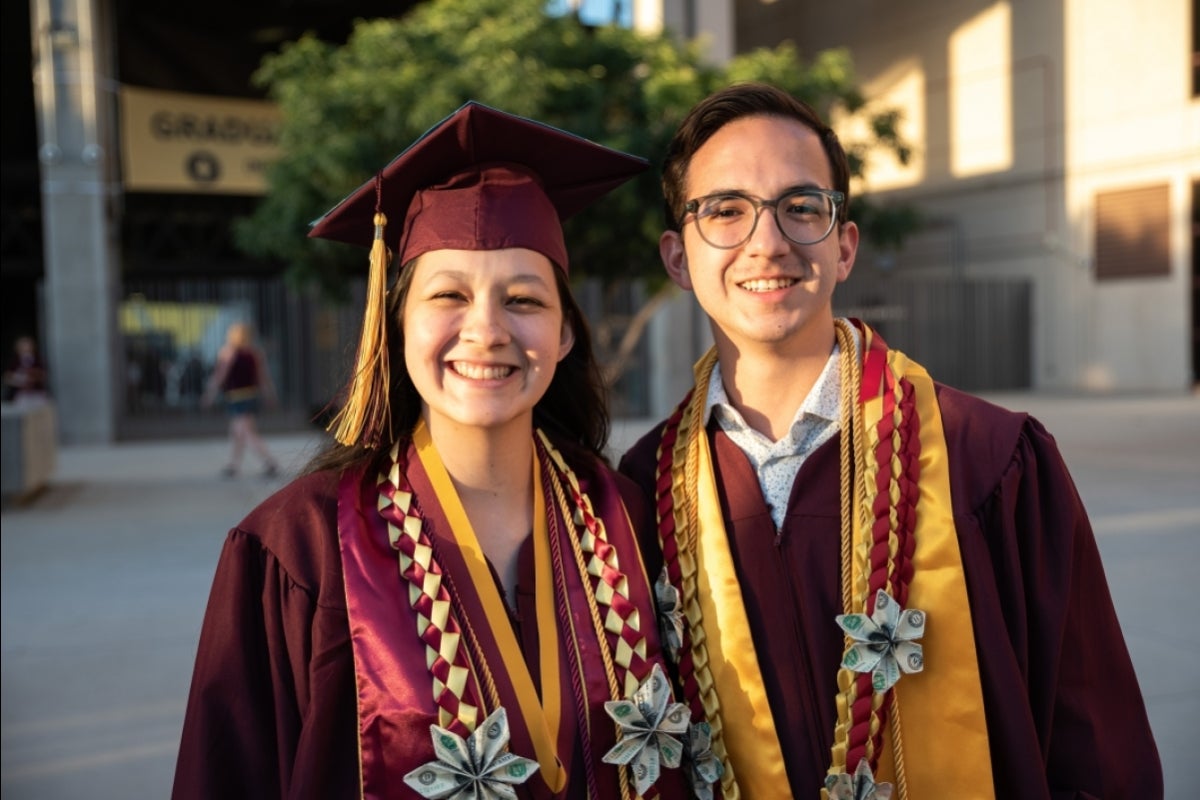 A woman and a man in graduation regalia pose for a photo