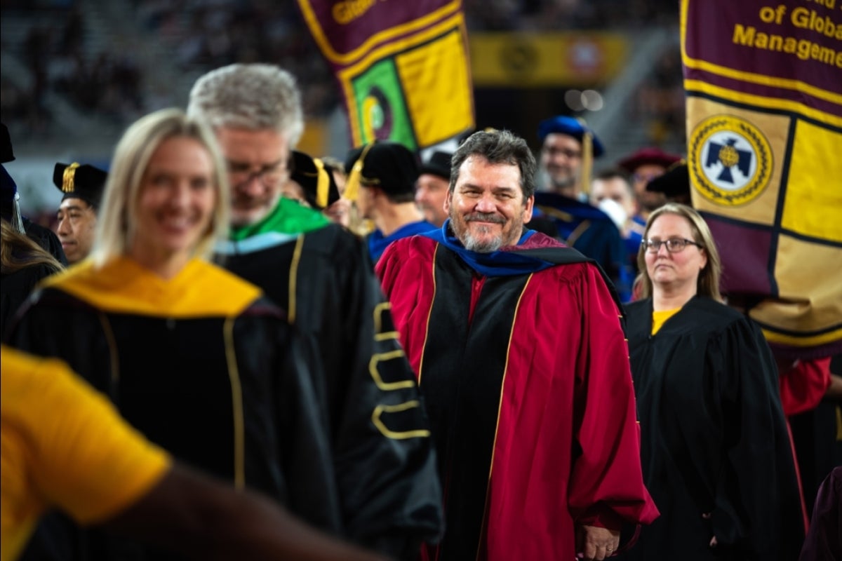 Faculty members in commencement regalia smile as they enter the ceremony