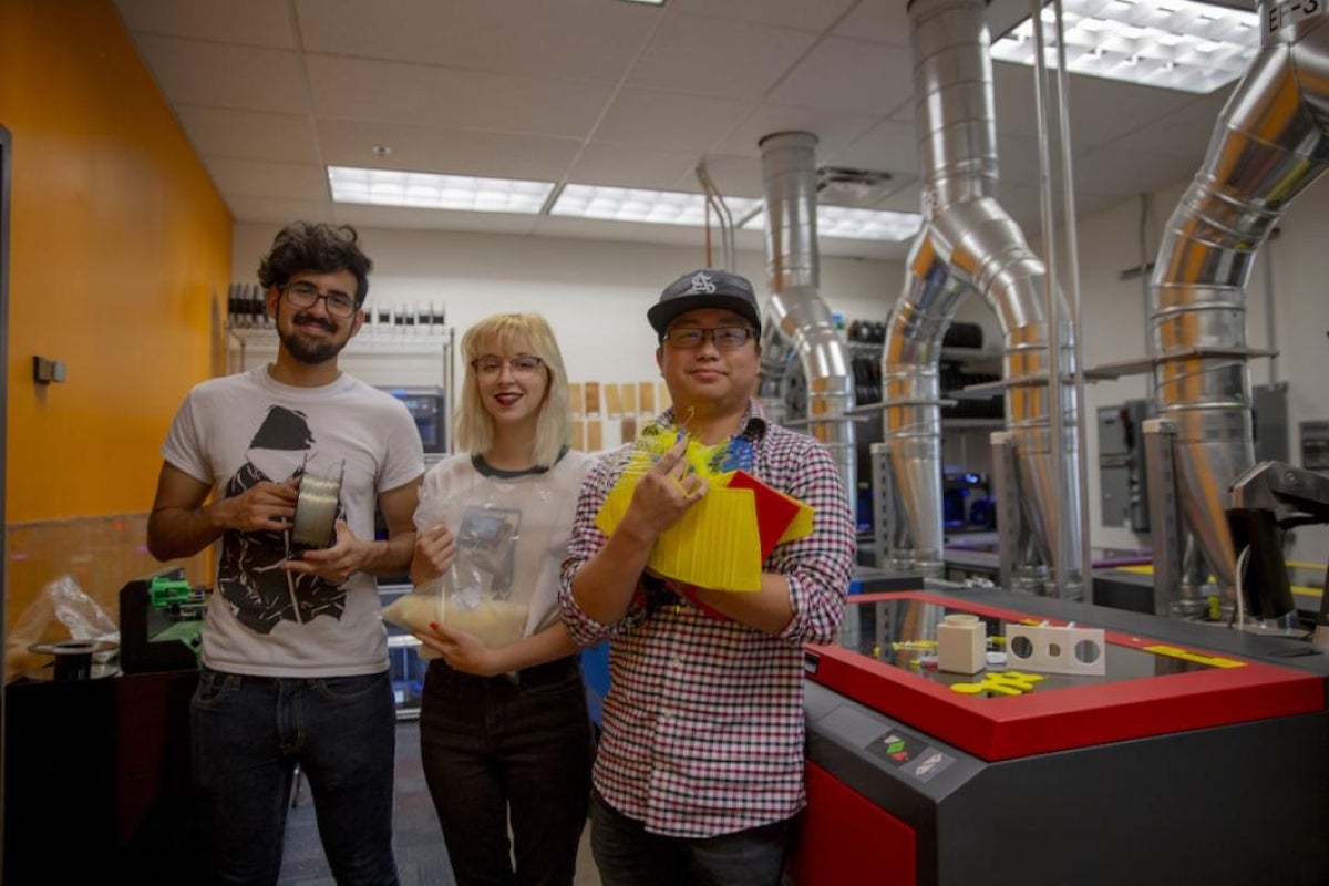 Three students hold items that represent different parts of the recycling process.