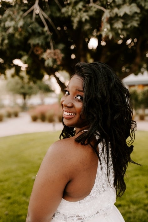 Abigail B. Fouts poses outdoors and looks over her shoulder in white dress.