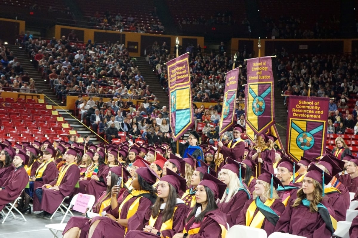 A group of graduates sit in the center of a full stadium.