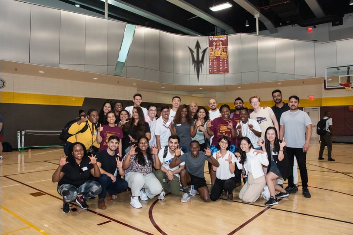 A group of students posing and smiling for a photo on an indoor basketball court.