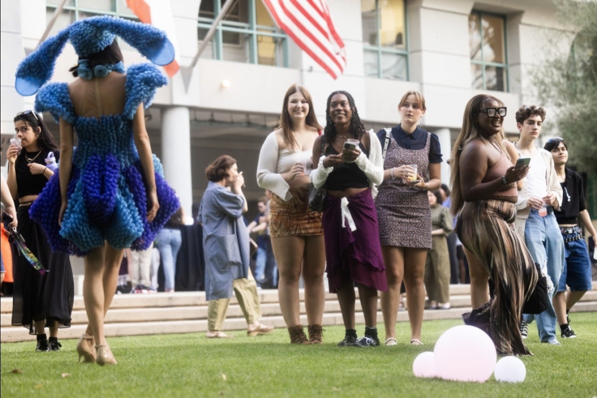 People watch model walk down lawn wearing blue design