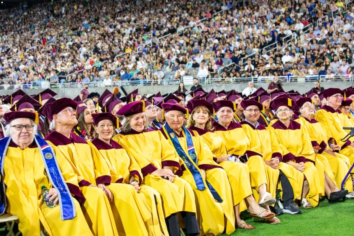 Golden Graduates sit together wearing gold graduation gowns and maroon caps.