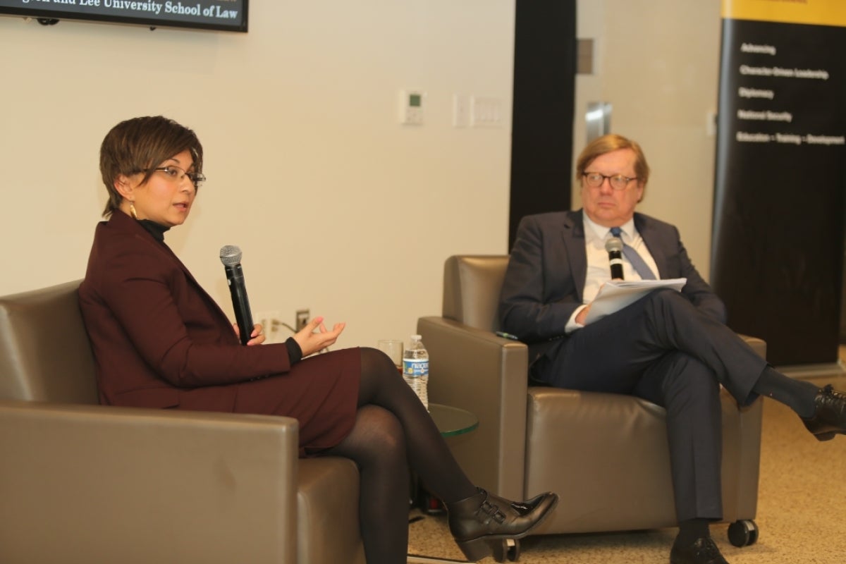 Kish Parella and David Scheffer sitting at chairs and holding microphones, with Parella speaking to an unseen audience.