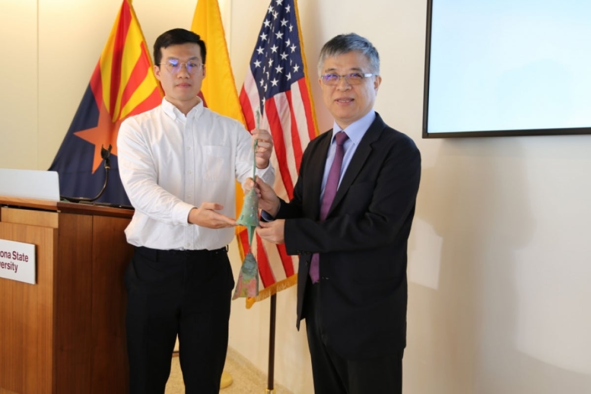 A young man presents a bell to an older man in a suit