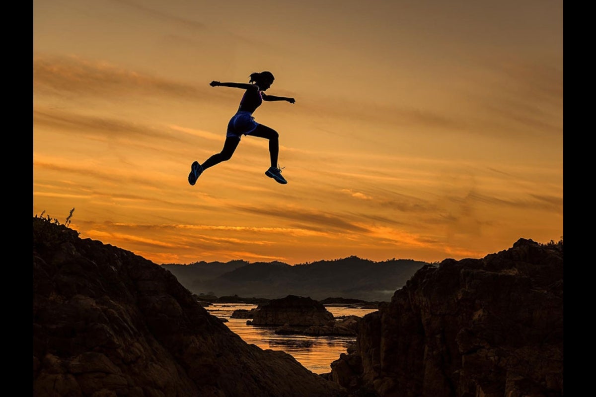 silhouette of person jumping across stream