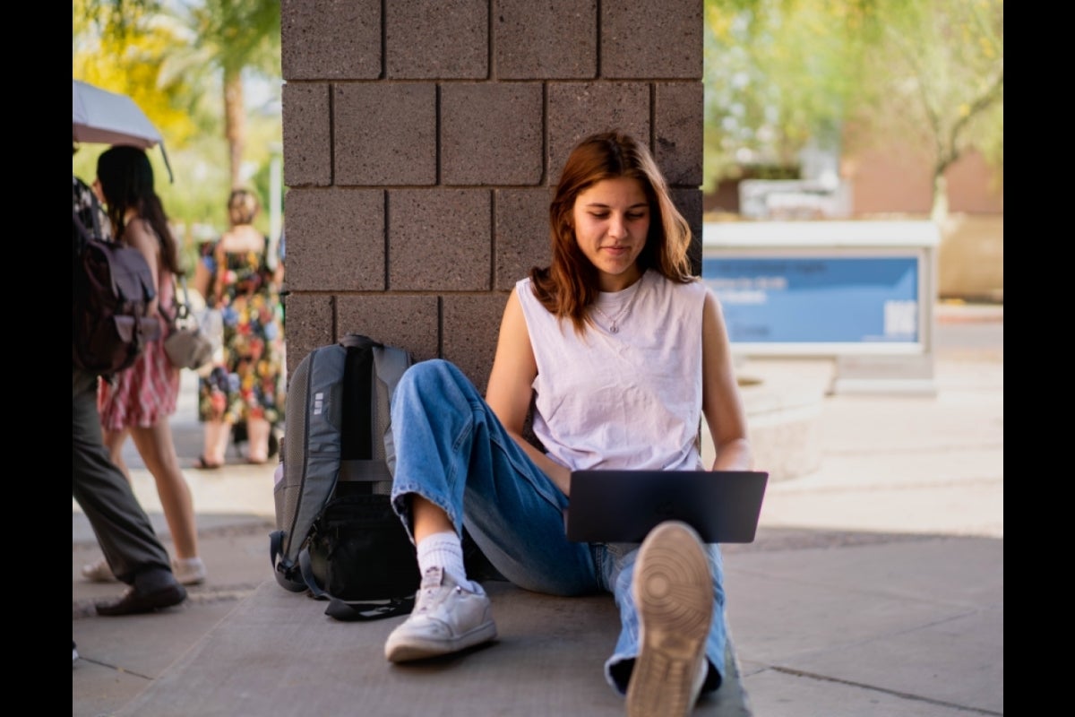 Person sitting with their back to the wall and looking down at the laptop in their lap.