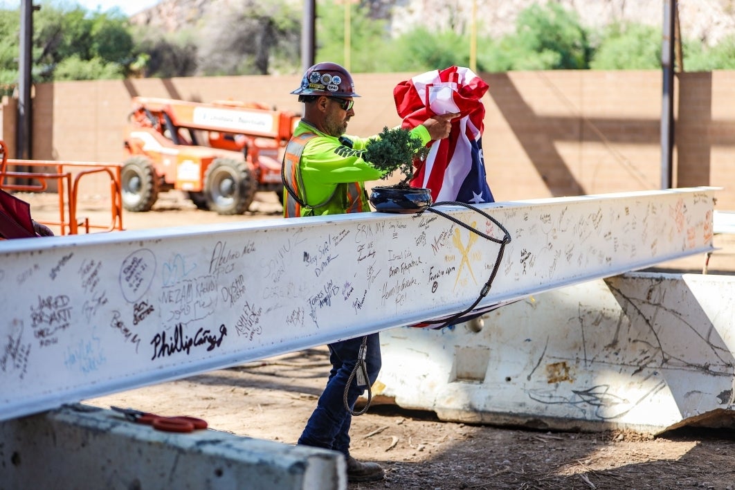 A construction worker hooks a US flag to a steel girder filled with signatures