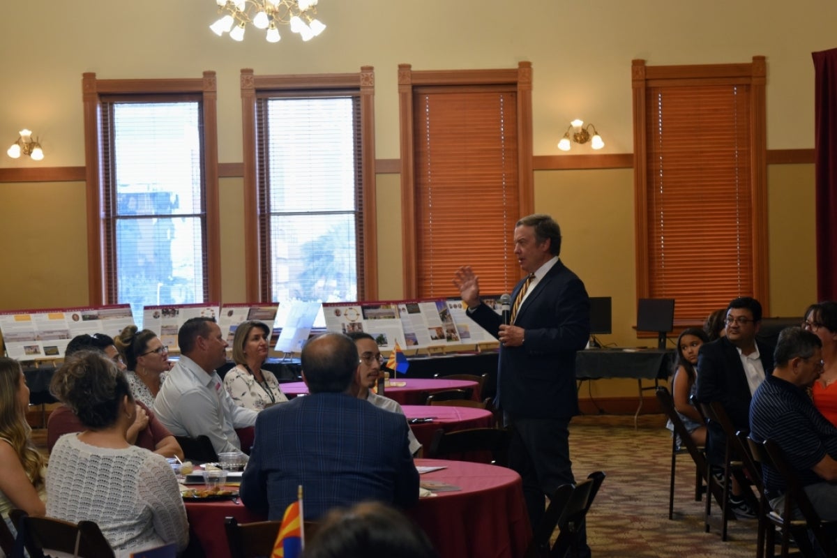 Michael Crow standing in front of a room of people sitting at tables.