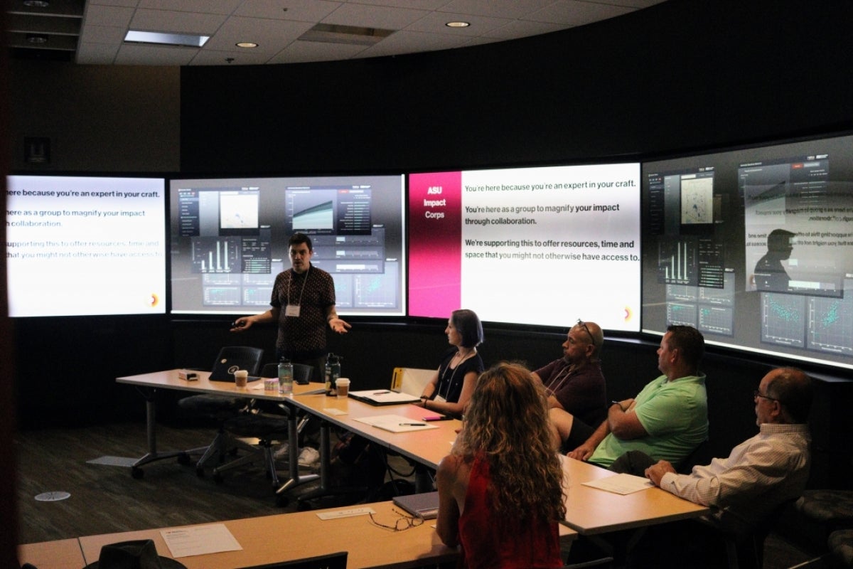 People sitting at a conference table with screens behind them.