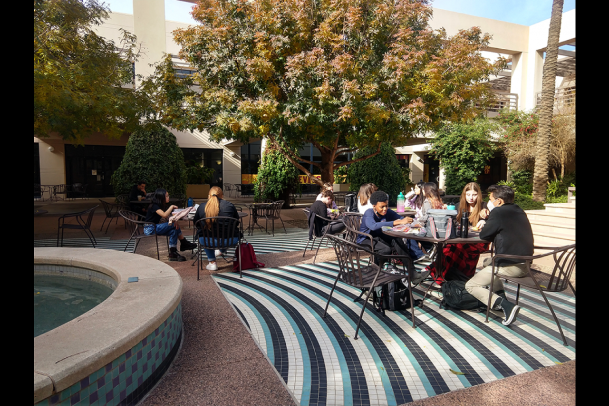 Group of high school students seated at a table in a courtyard.