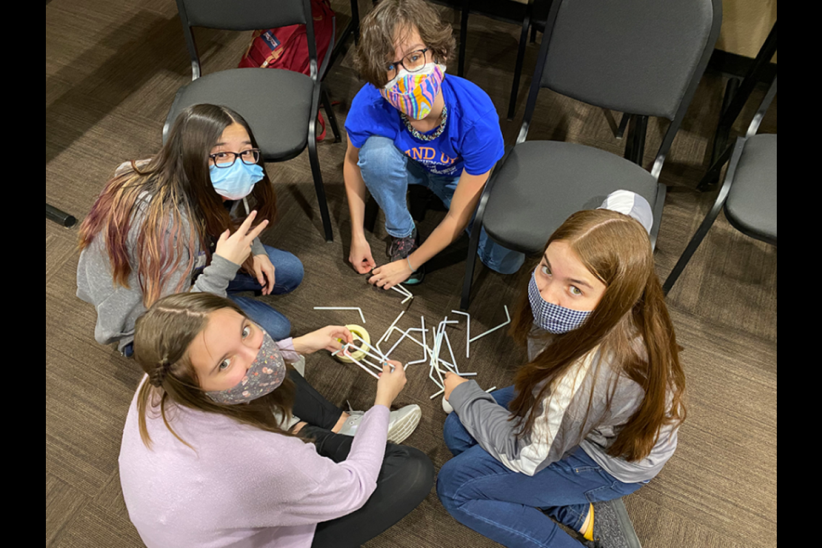 Students seated in a circle on the floor look up at the camera.