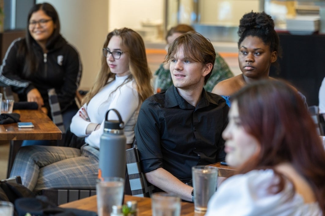 Several students seated at tables looking toward an unseen speaker.