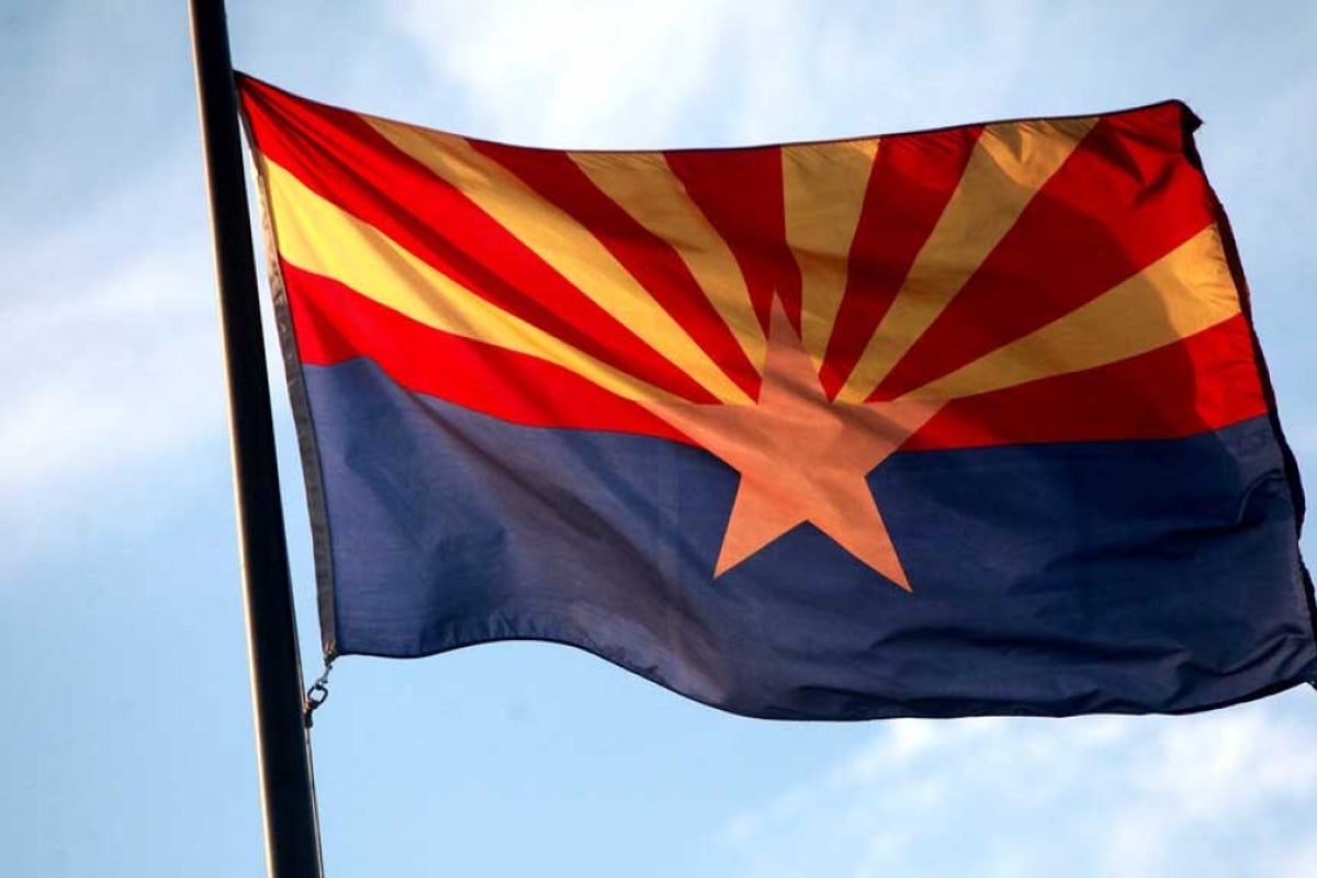 The Arizona state flag on a flagpole and backlit by the sun