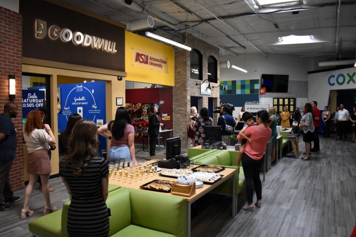 People gathered in a space with mock storefronts.