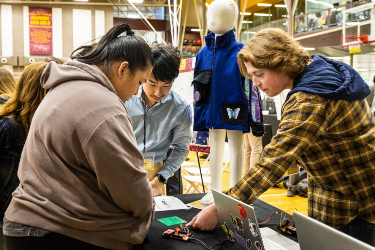 Students lean over a table, looking at a device.