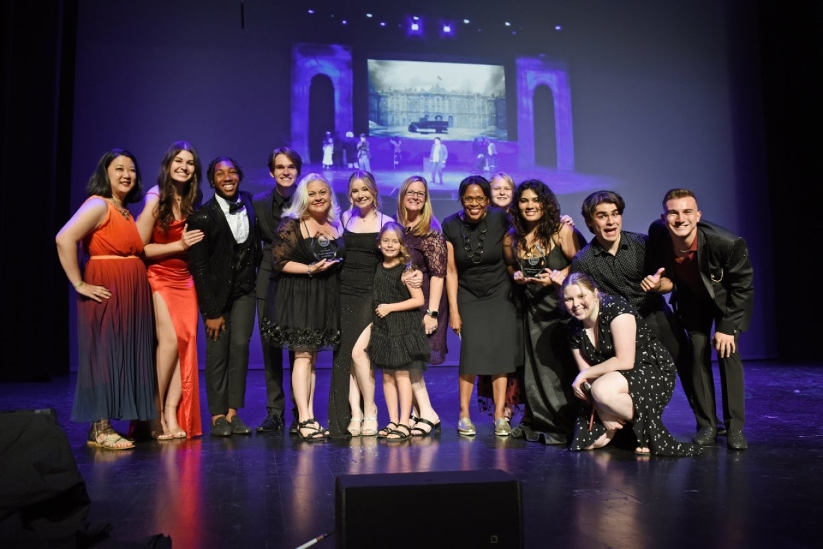 A group of performers in formal wear stand on a stage for a photo.