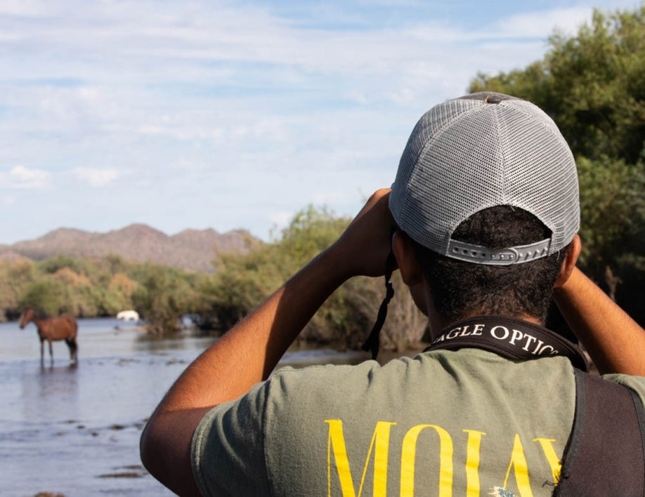 Student looking at horses on the river with binoculars