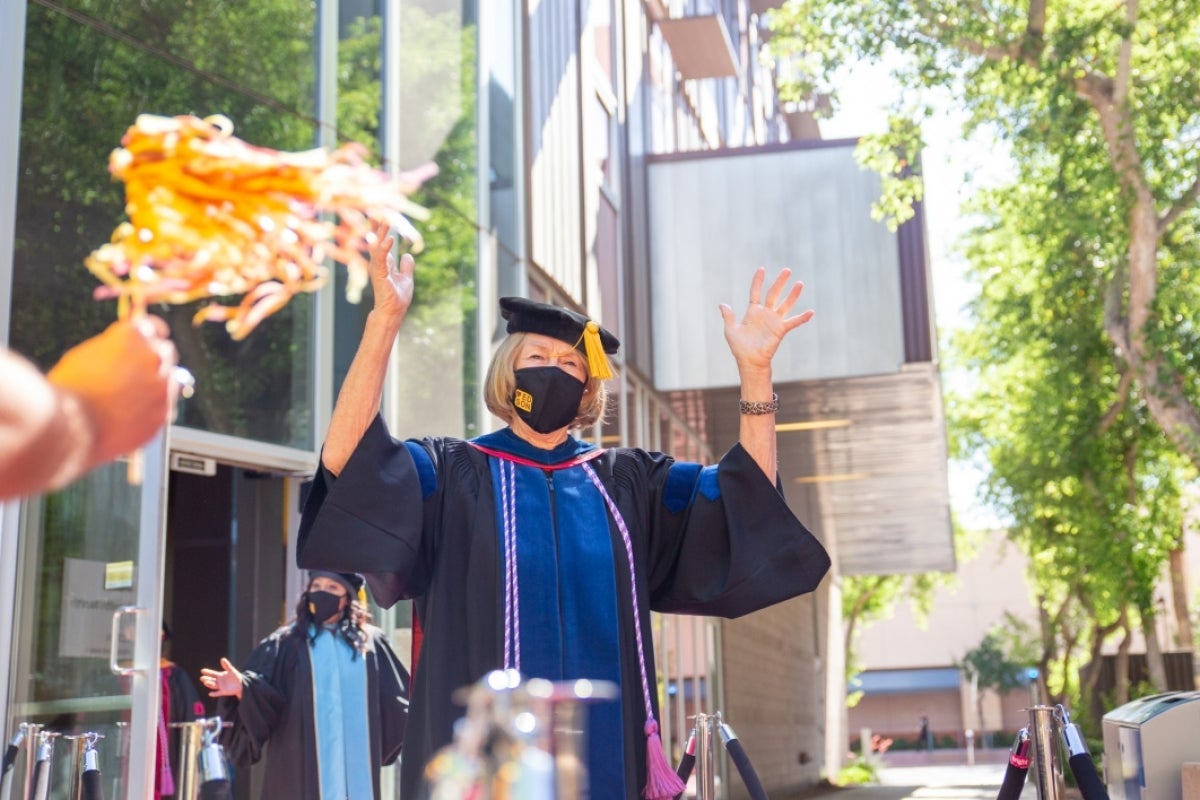 A woman in graduation regalia waves