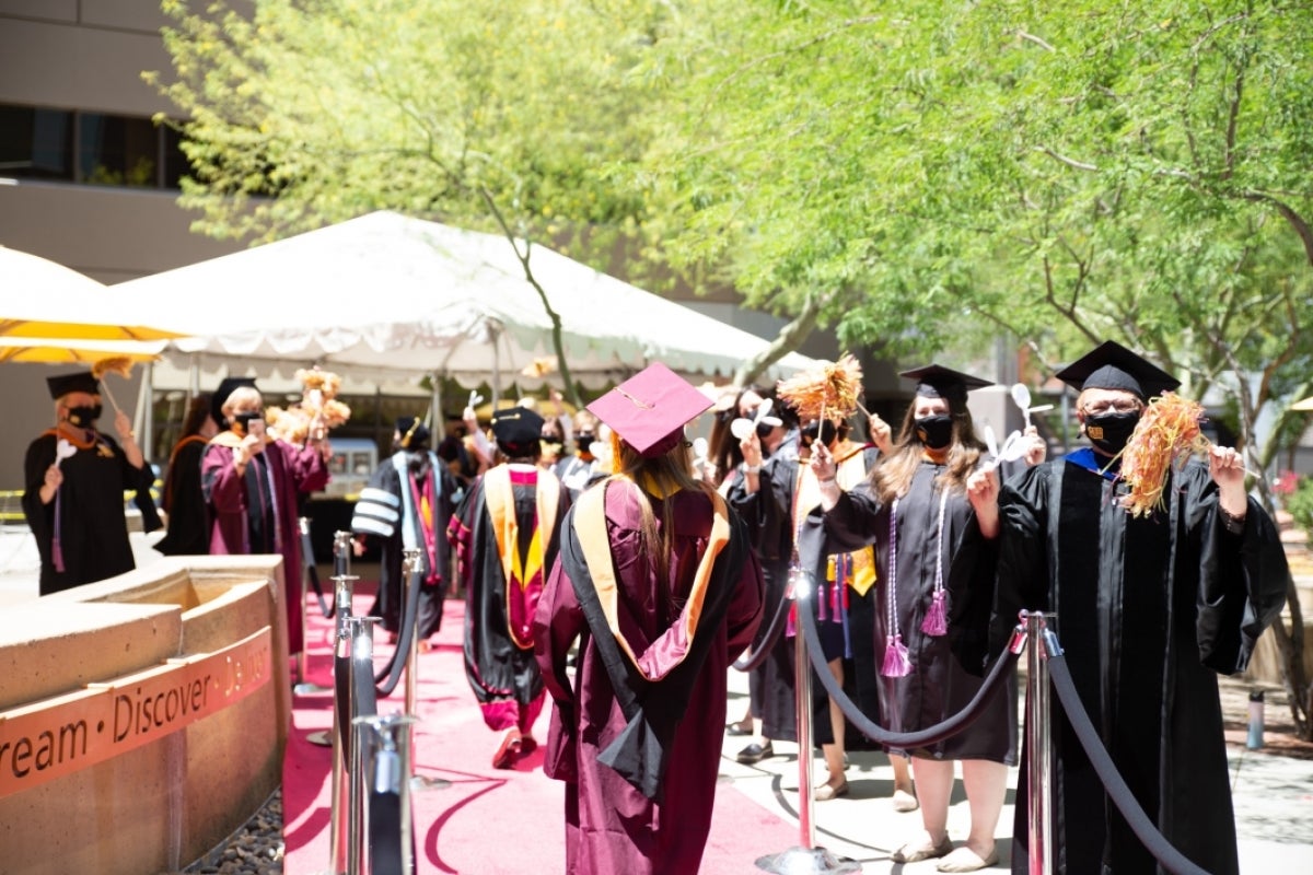 Graduating students walk through a roped off walkway while being cheered on by faculty in graduation regalia