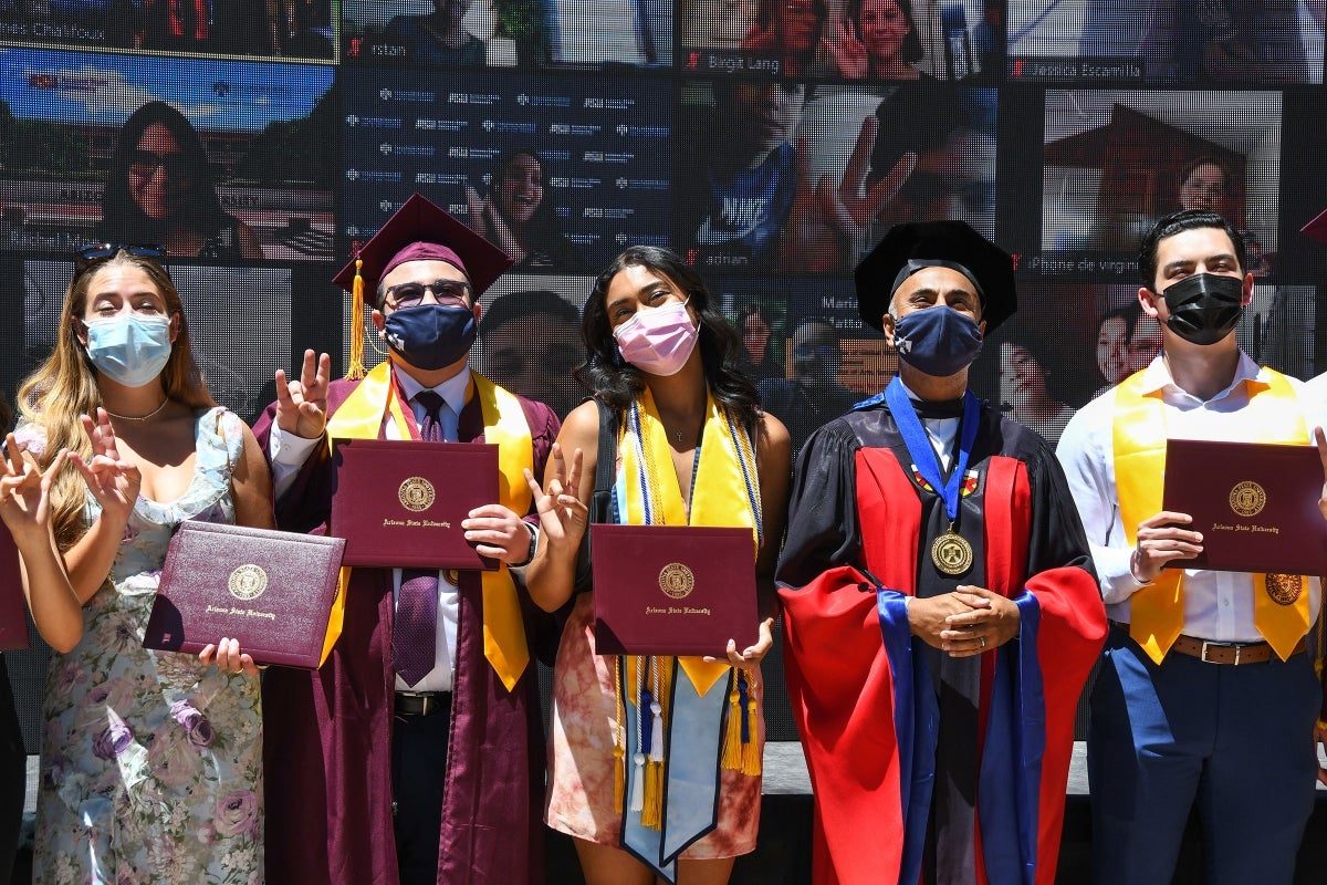 Graduating students stand with the Thunderbird dean in front of a giant Zoom wall