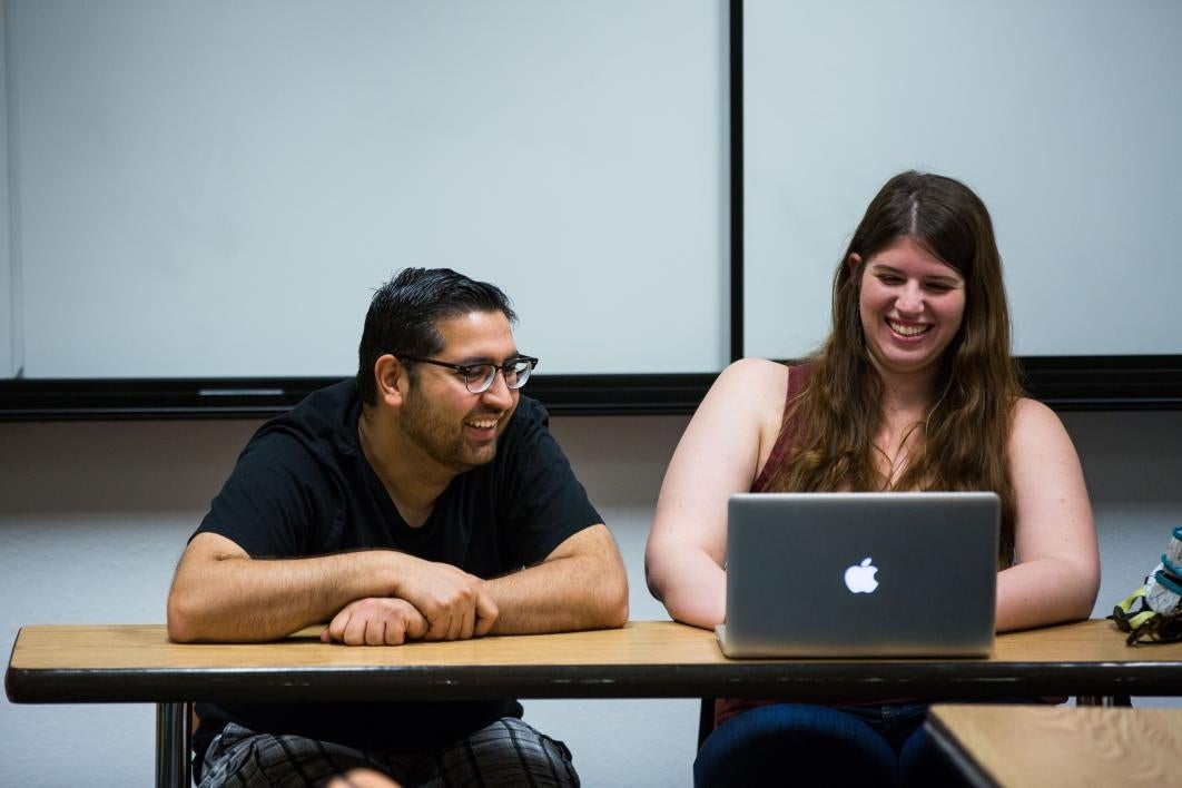 two student editors talking and looking at latptops