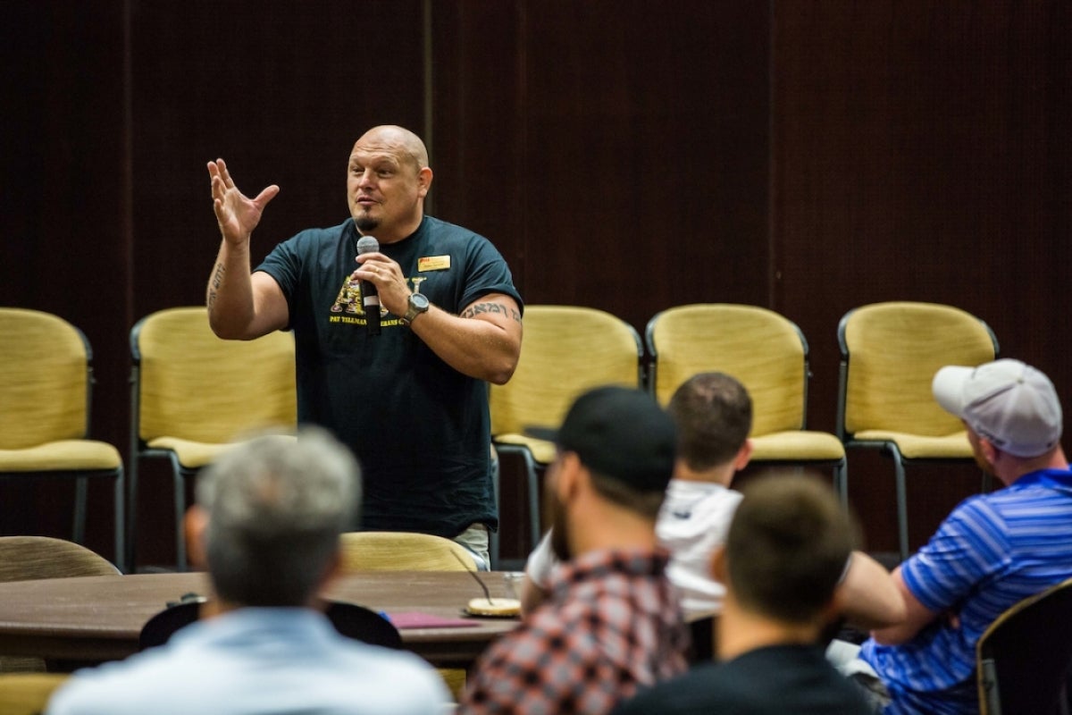 Man holding a microphone and speaking to a crowd in an auditorium.