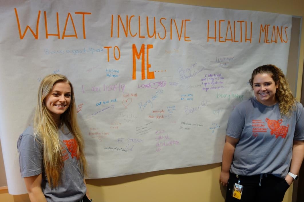 Students Meghan Henrichsen and Jessie Arnett pose next to the social wellness station