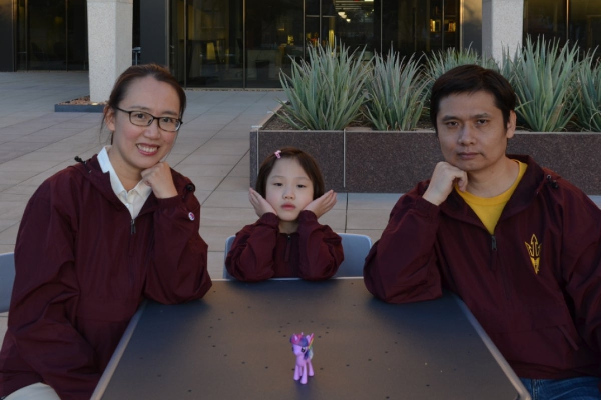 Two parents and a little girl sit at a table looking at the camera