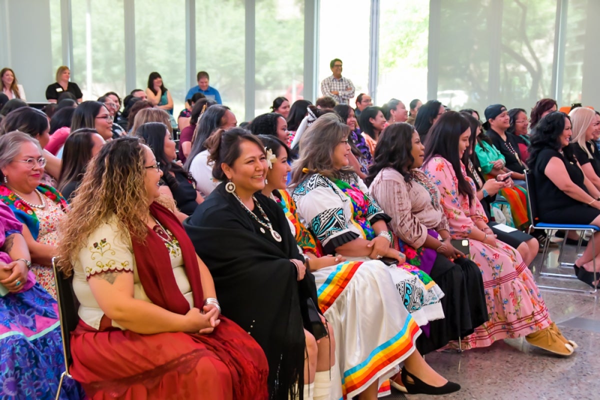 A group of women sit in lined up chairs as an audience.