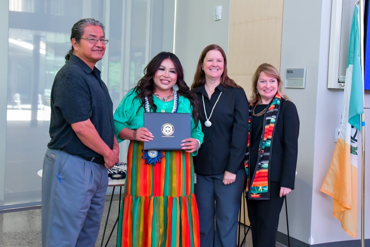 Veronda J. Hills stands posing for a photo with others and holding a diploma with