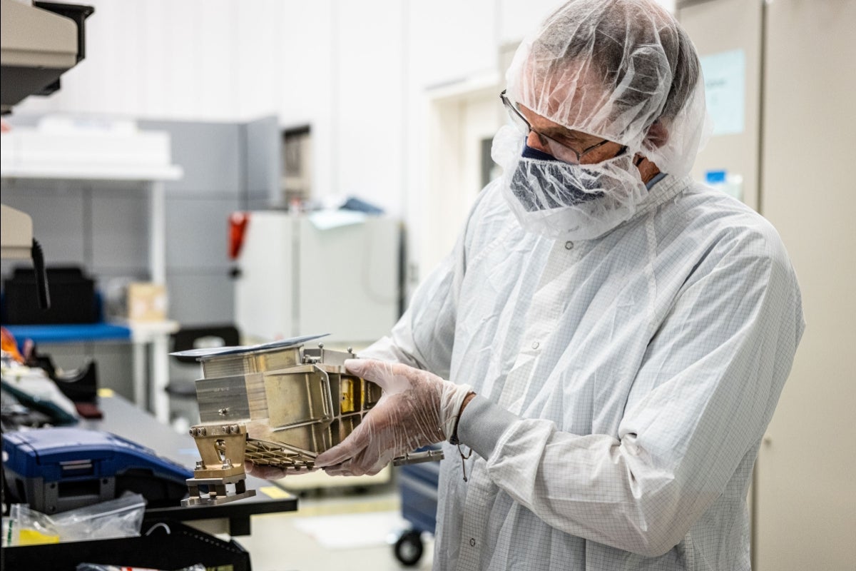 A man in a lab coat holds a piece of metal imaging equipment