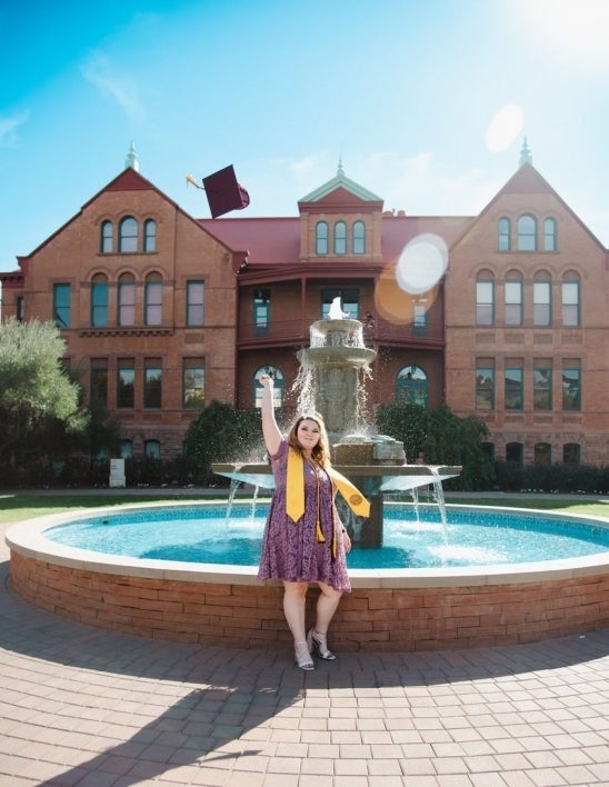 woman wearing graduation stole, standing in front of fountain