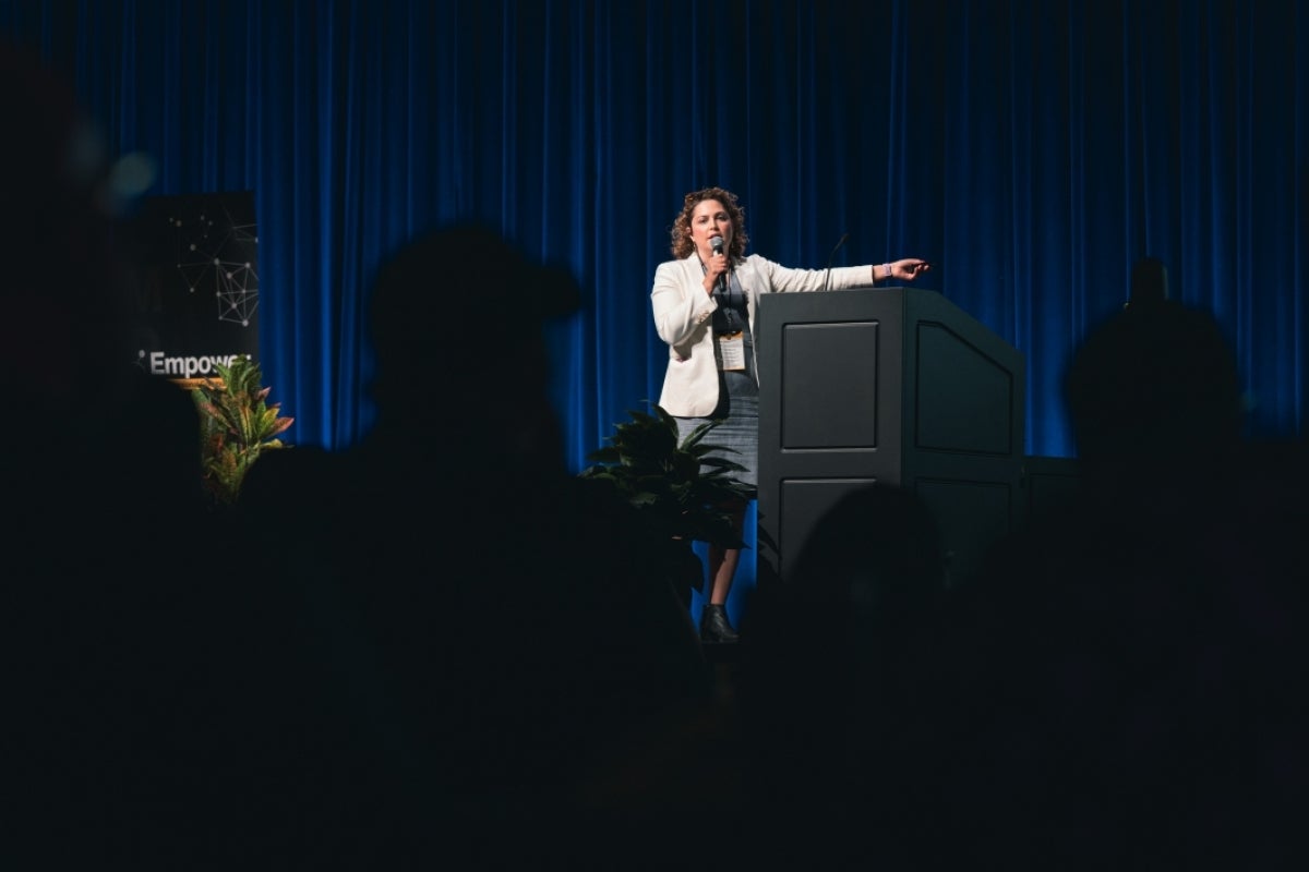 Laura Pol standing by a podium with a microphone.