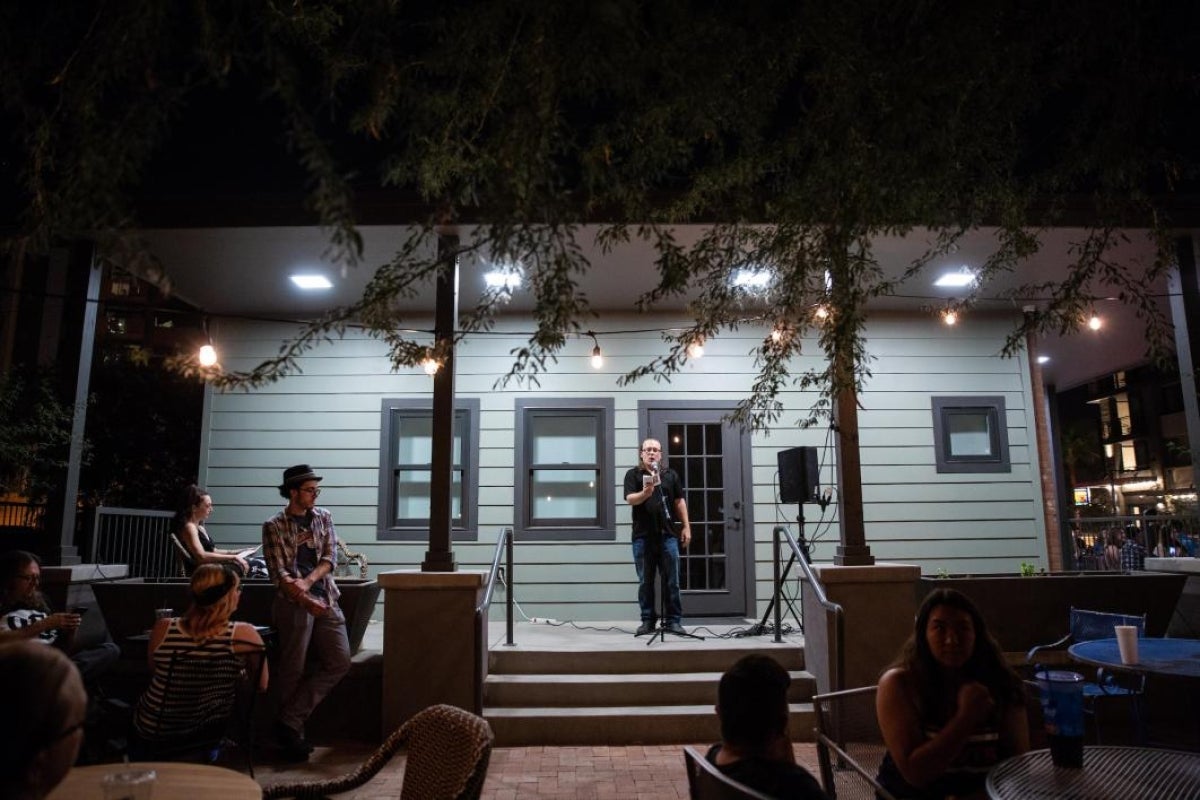 man speaking to crowd from porch of a house at night