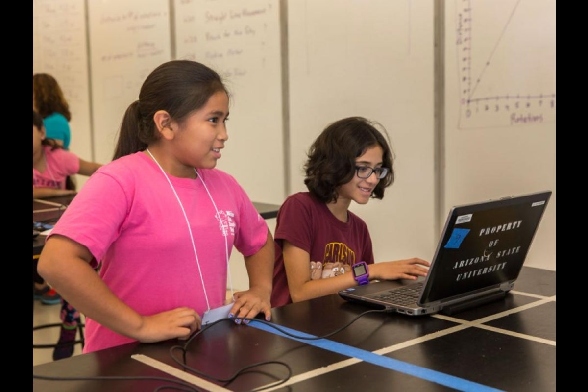 Two girls work at a laptop to program their robot.