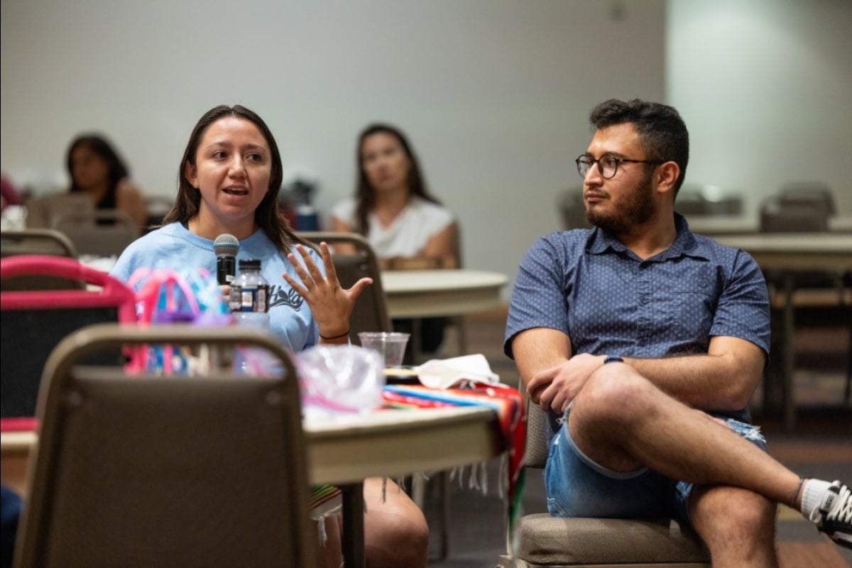 Woman speaking into a microphone while a man seated next to her listens.