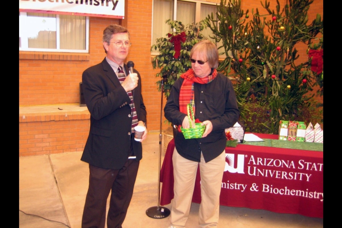 Man speaking into a microphone while another man stands next to him.