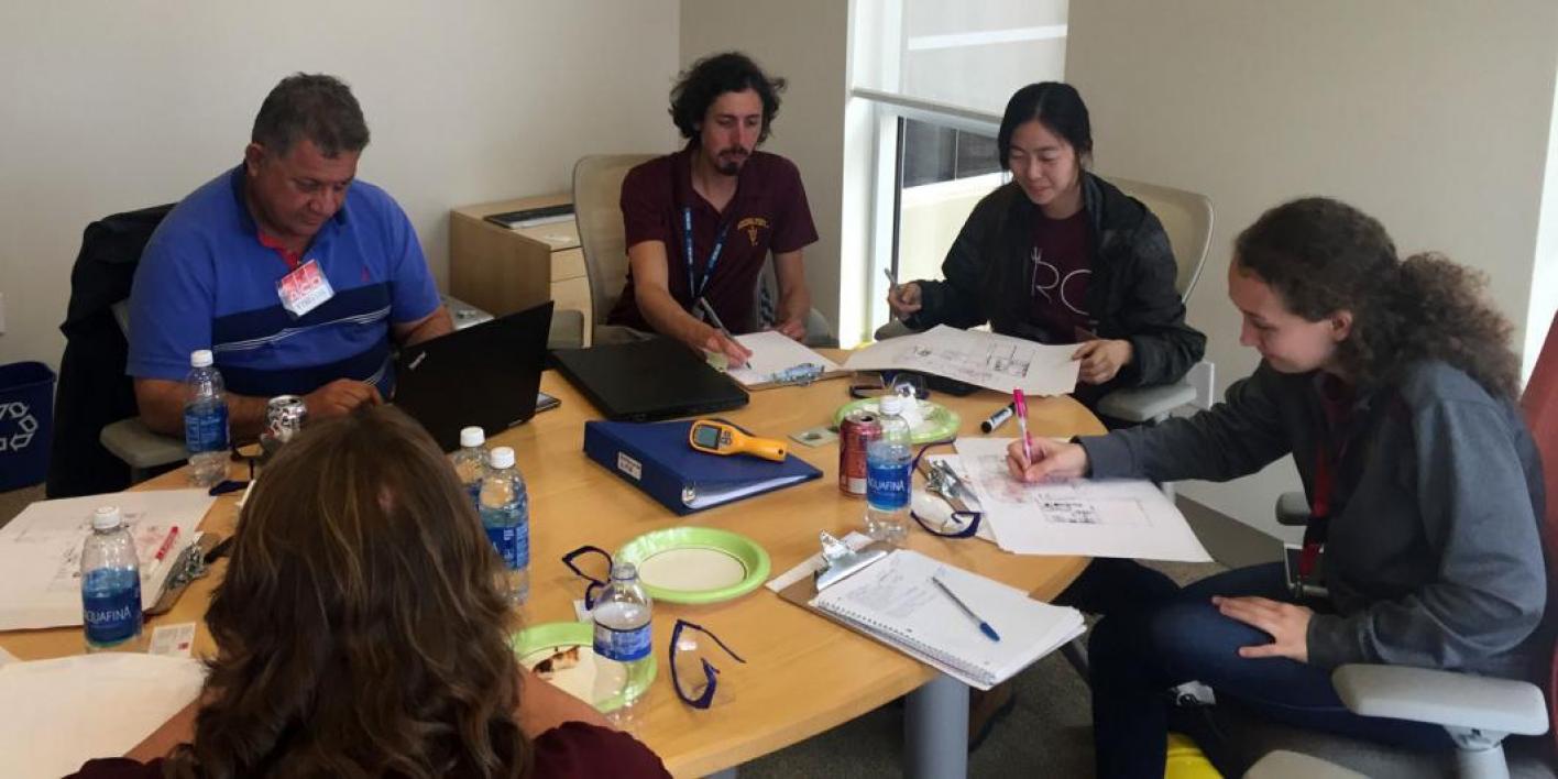 This photo shows a team of students sitting at a table analyzing data from their on-site visit of a manufacturing center.