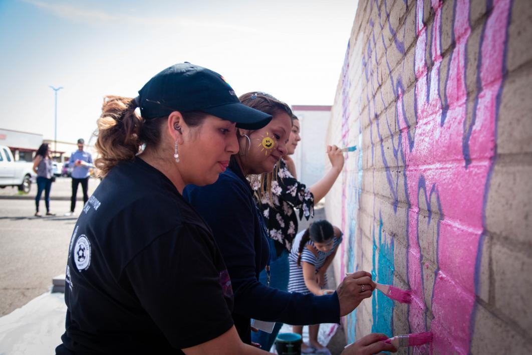 Community members, including adults and kids, a giant pink hand with a heart in the center on a brick wall at the event