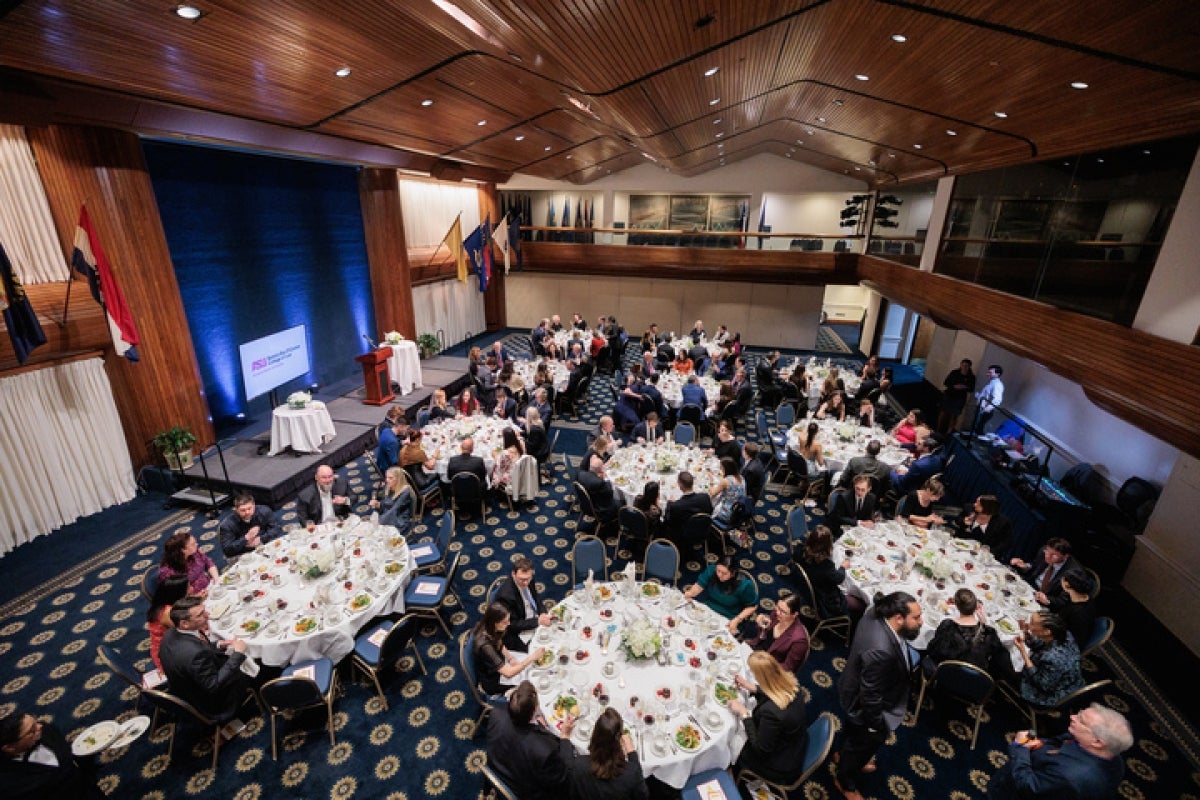 A crowd of guests are seated at white cloth tables.