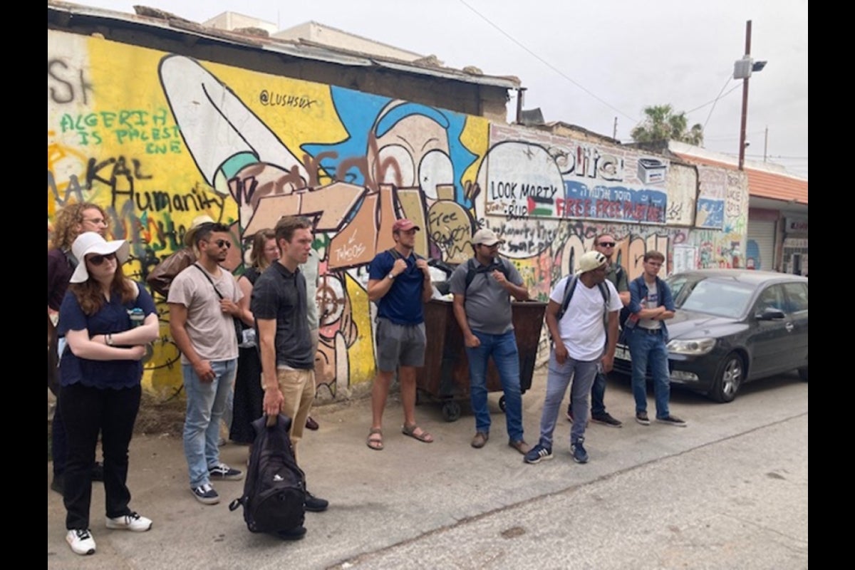 Student stand in front of graffitied wall in Israel