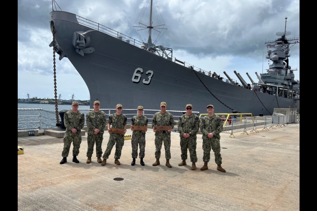 Navy sailors pose in front of a battleship.