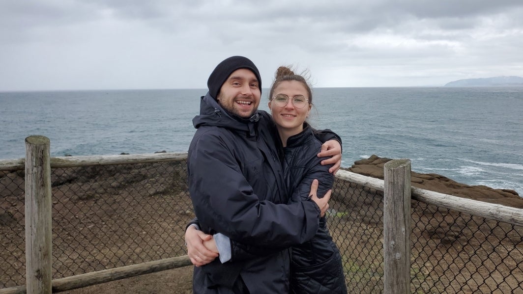 Sasha Sharstniou and his wife Aksana Atrashkevich pose for a photo in front of a body of water.