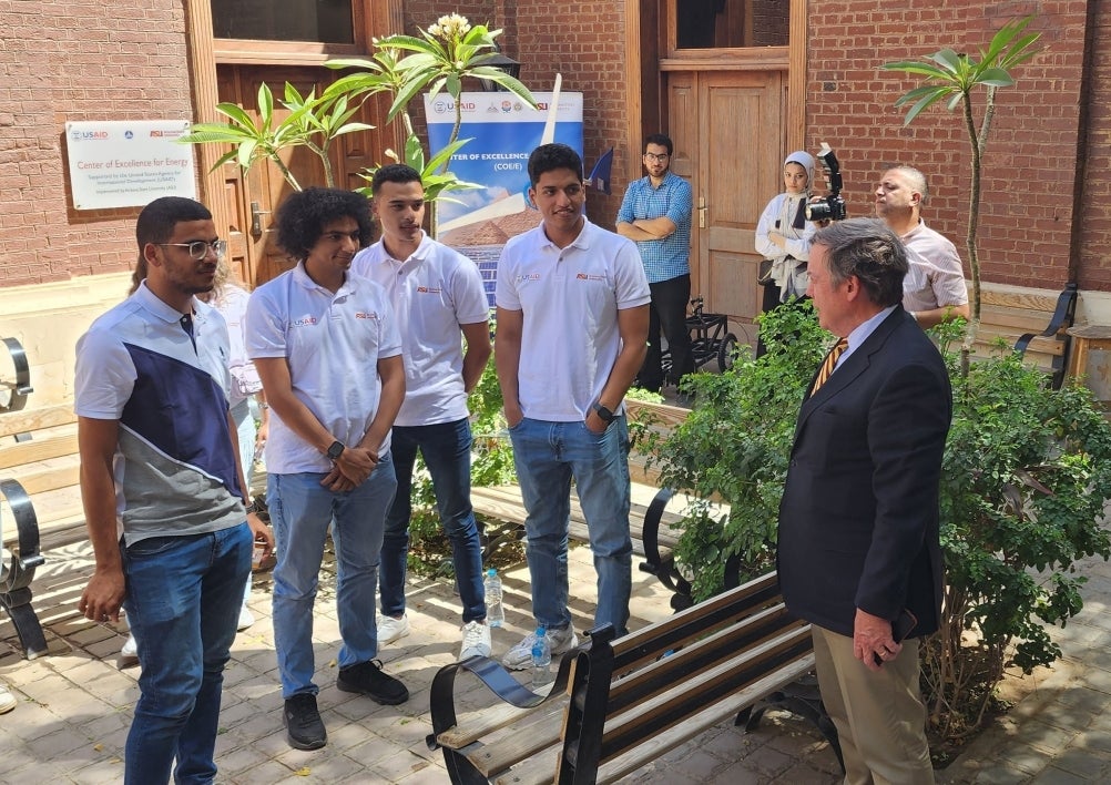 A man in a suit speaks with a group of college students