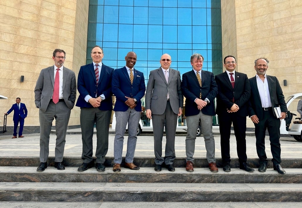 Seven men in suits pose for a group photo on steps