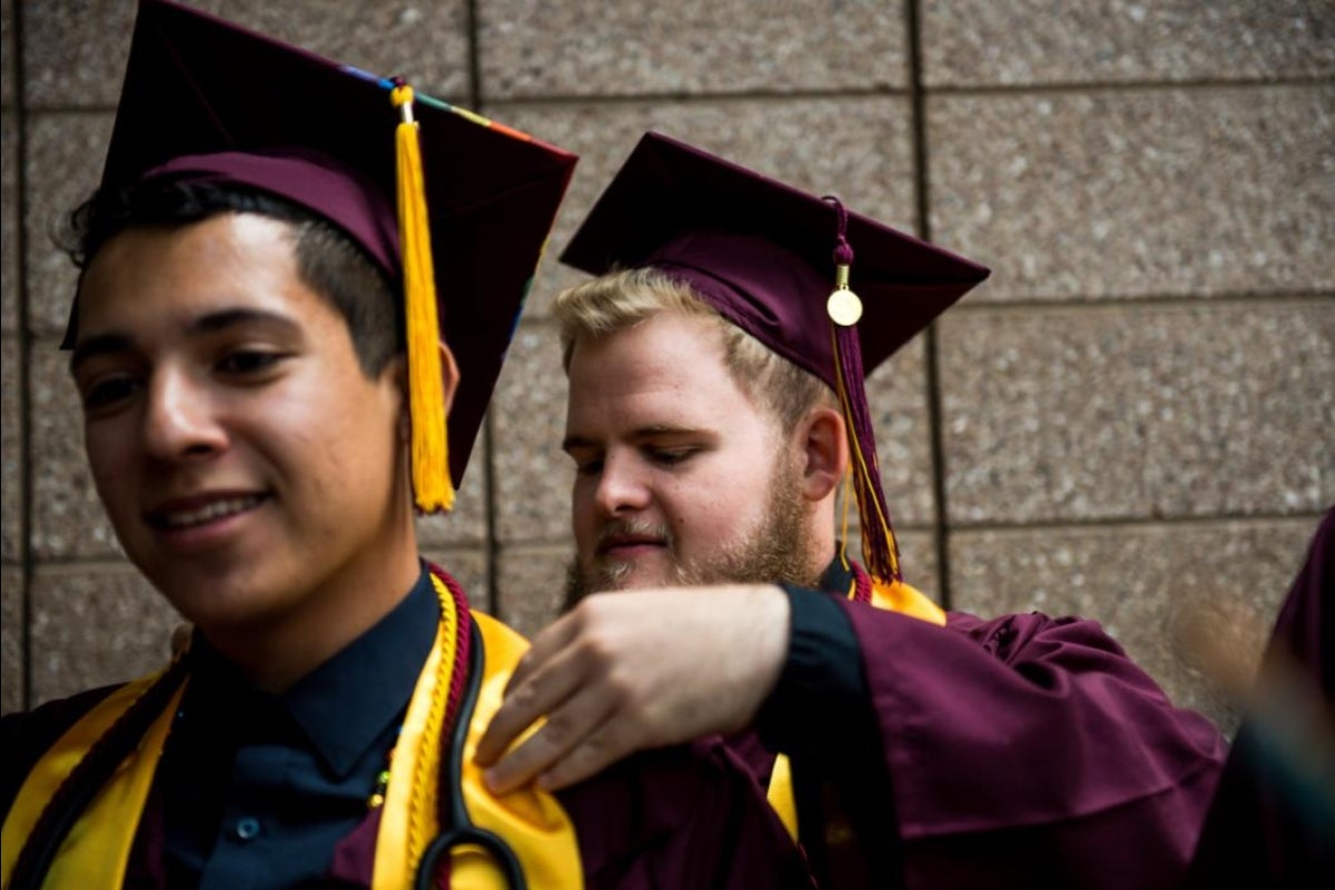 graduate adjusting cords on other graduate's gown